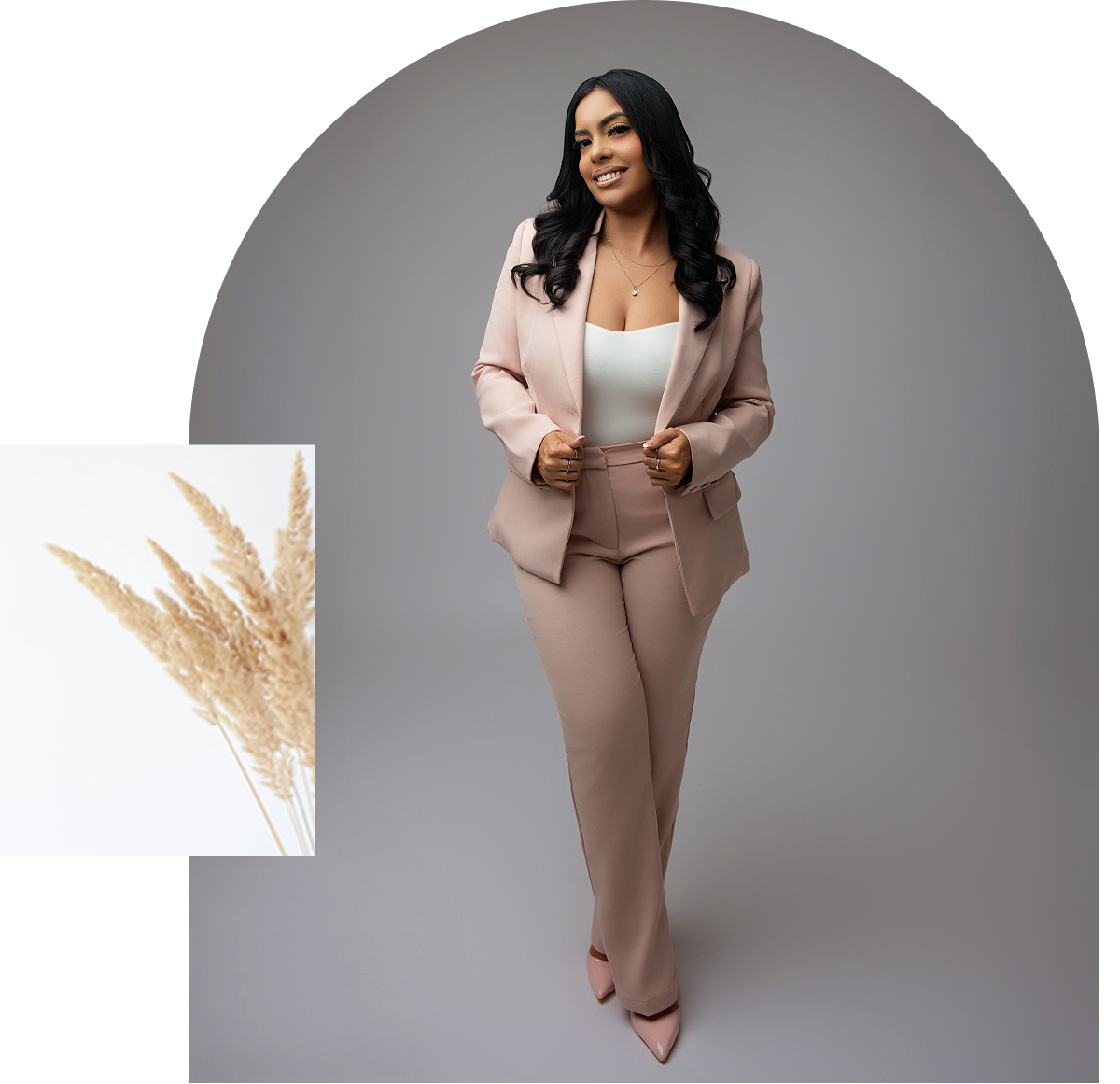 A woman in a stylish pink suit with a white top poses confidently against a gray background.