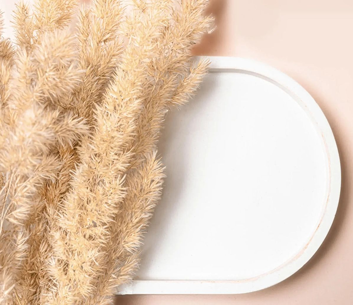 Soft beige pampas grass next to a white oval tray on a light surface.
